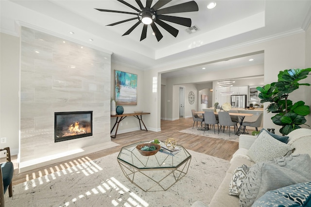 living room featuring wood-type flooring, a tile fireplace, crown molding, and a raised ceiling