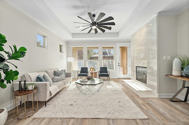 living room with light hardwood / wood-style flooring, ceiling fan, a tray ceiling, a premium fireplace, and ornamental molding