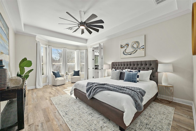 bedroom featuring ceiling fan, a tray ceiling, ornamental molding, and light wood-type flooring