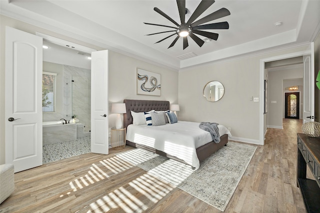 bedroom with light hardwood / wood-style flooring, connected bathroom, a tray ceiling, and ceiling fan