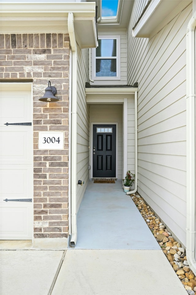 entrance to property featuring a garage and brick siding