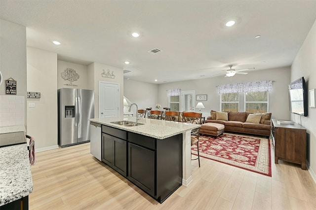 kitchen featuring light stone countertops, appliances with stainless steel finishes, an island with sink, light hardwood / wood-style floors, and sink