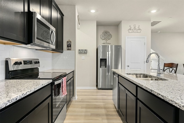 kitchen featuring visible vents, appliances with stainless steel finishes, light stone counters, dark cabinetry, and a sink