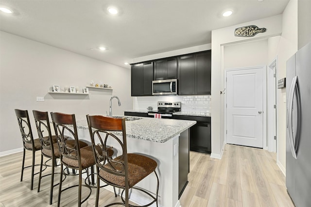 kitchen with a center island with sink, stainless steel appliances, a sink, dark cabinetry, and a kitchen breakfast bar