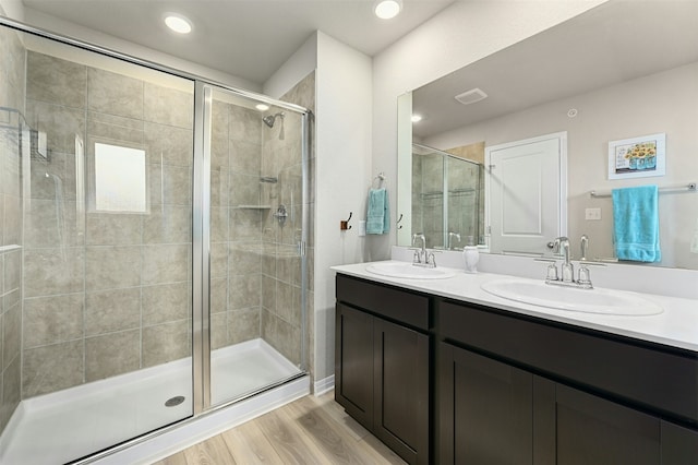 bathroom featuring double vanity, wood finished floors, a sink, and a shower stall