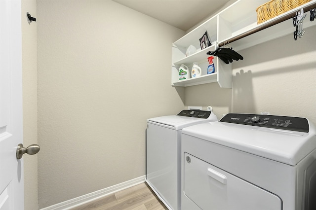 washroom with light wood-type flooring, laundry area, baseboards, and washing machine and clothes dryer