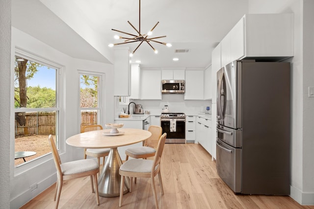 kitchen featuring white cabinets, stainless steel appliances, light hardwood / wood-style floors, sink, and a notable chandelier