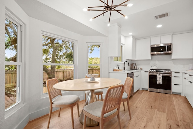 kitchen with appliances with stainless steel finishes, white cabinetry, tasteful backsplash, sink, and light hardwood / wood-style flooring