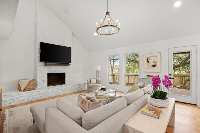 living room featuring light hardwood / wood-style floors, a notable chandelier, high vaulted ceiling, and a stone fireplace