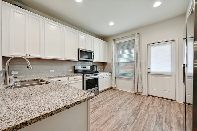 kitchen featuring light stone countertops, white cabinets, appliances with stainless steel finishes, sink, and light hardwood / wood-style flooring