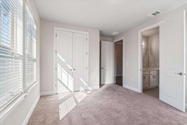 unfurnished bedroom featuring light colored carpet, a closet, and ensuite bathroom