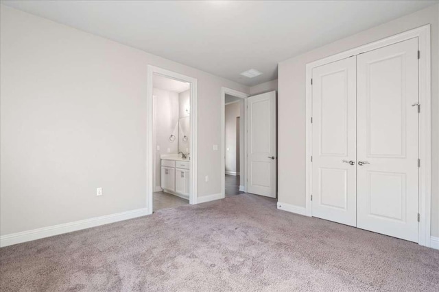 unfurnished bedroom with a closet, ensuite bathroom, light colored carpet, and sink