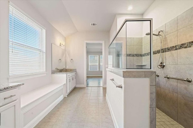 bathroom with a tile shower, vaulted ceiling, tile patterned floors, and vanity