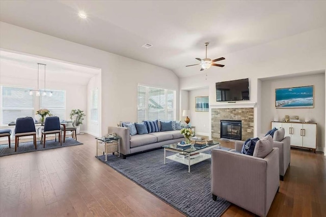 living room with ceiling fan, dark hardwood / wood-style floors, lofted ceiling, and a stone fireplace