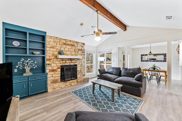 living room with a stone fireplace, light hardwood / wood-style floors, a textured ceiling, vaulted ceiling with beams, and ceiling fan