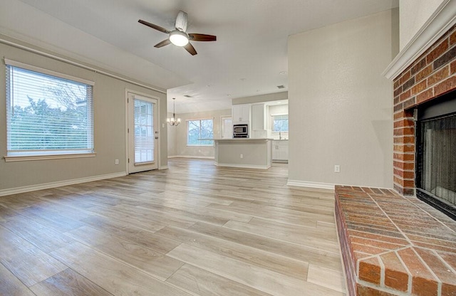 unfurnished living room with light wood-type flooring, ceiling fan with notable chandelier, and a brick fireplace