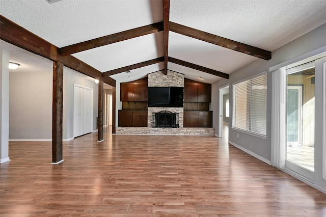 unfurnished living room featuring light hardwood / wood-style floors, a textured ceiling, lofted ceiling with beams, and a stone fireplace