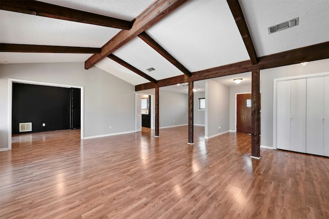 unfurnished living room with vaulted ceiling with beams, light hardwood / wood-style floors, and a textured ceiling