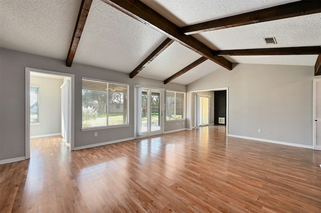 unfurnished living room with wood-type flooring, a textured ceiling, and lofted ceiling with beams