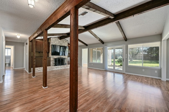 unfurnished living room featuring wood-type flooring, a wealth of natural light, a stone fireplace, and vaulted ceiling with beams