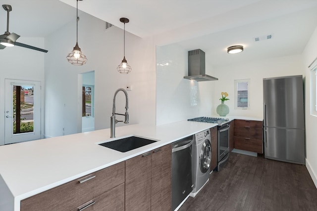 kitchen with washer / dryer, appliances with stainless steel finishes, sink, kitchen peninsula, and wall chimney exhaust hood