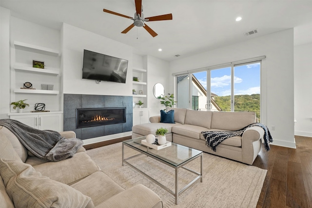 living room with built in features, hardwood / wood-style floors, a tiled fireplace, and ceiling fan