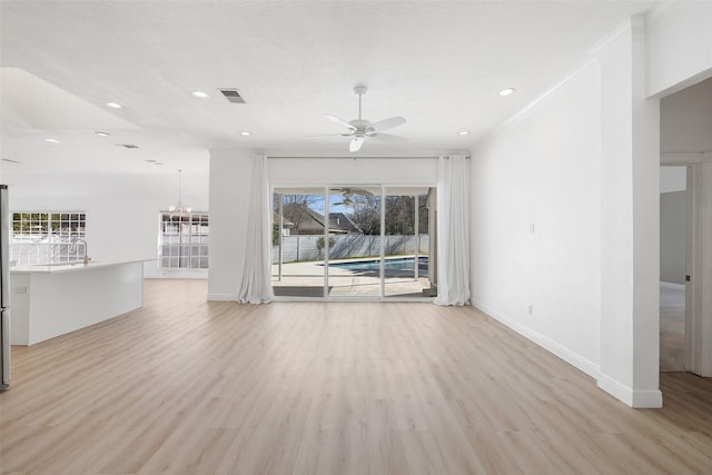 unfurnished living room with ceiling fan with notable chandelier, crown molding, and light wood-type flooring