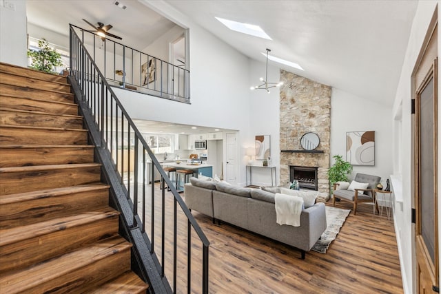 living room with a skylight, hardwood / wood-style floors, high vaulted ceiling, and a stone fireplace