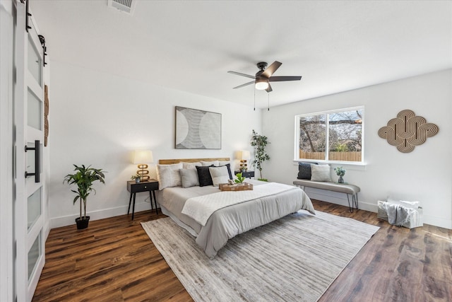 bedroom featuring ceiling fan, dark hardwood / wood-style floors, and a barn door