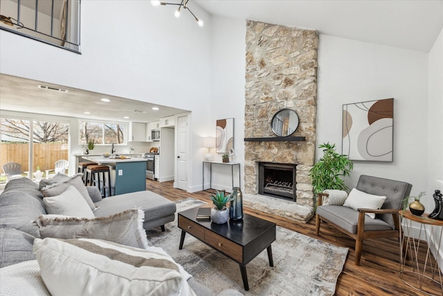 living room with a stone fireplace, hardwood / wood-style floors, and high vaulted ceiling