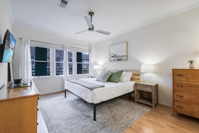 bedroom with light wood finished floors, visible vents, ornamental molding, a ceiling fan, and baseboards