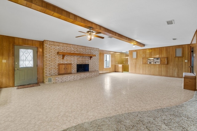 unfurnished living room with ceiling fan, beamed ceiling, wood walls, and a fireplace