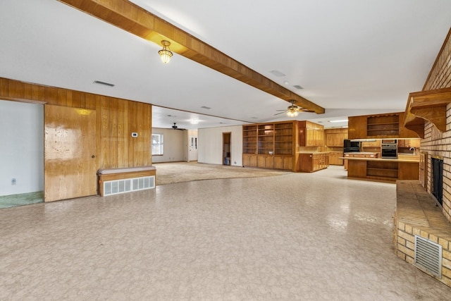 unfurnished living room featuring a fireplace, wooden walls, vaulted ceiling with beams, and ceiling fan