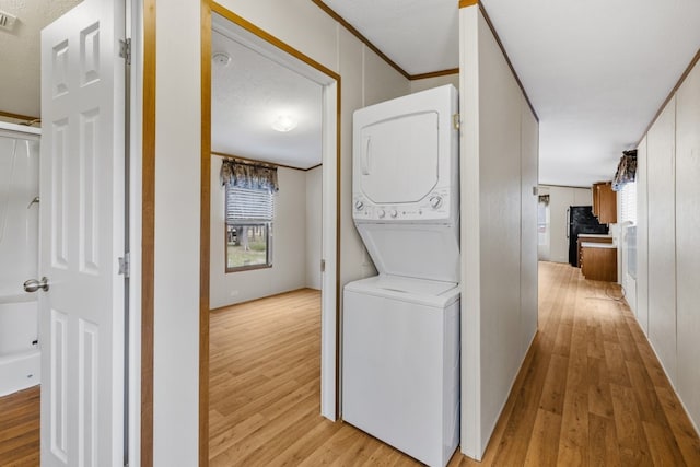 clothes washing area featuring crown molding, light wood-type flooring, a textured ceiling, and stacked washer and clothes dryer