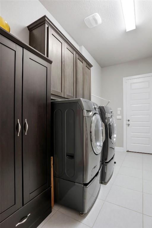 laundry room featuring washing machine and dryer, a textured ceiling, light tile patterned floors, and cabinets