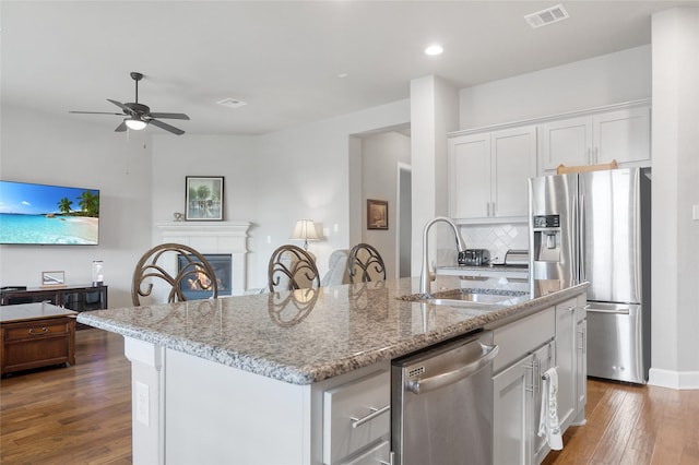 kitchen with light stone countertops, appliances with stainless steel finishes, sink, white cabinets, and an island with sink