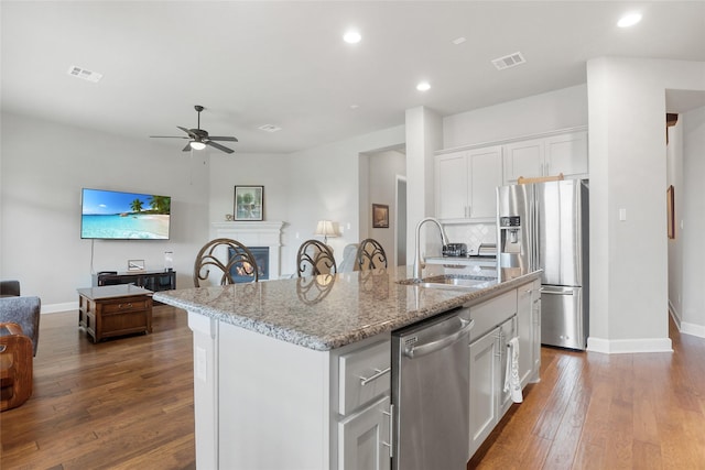 kitchen featuring appliances with stainless steel finishes, sink, white cabinetry, light stone counters, and a center island with sink