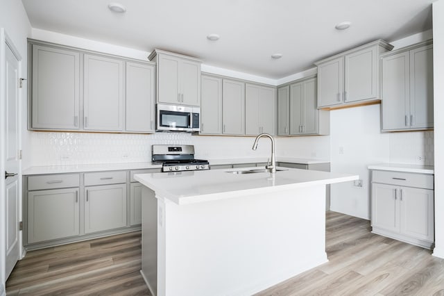 kitchen featuring sink, gray cabinets, stainless steel appliances, and a center island with sink