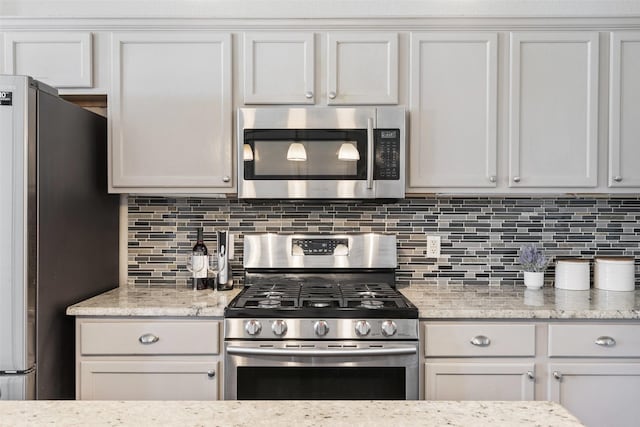 kitchen featuring white cabinets, backsplash, light stone counters, and appliances with stainless steel finishes