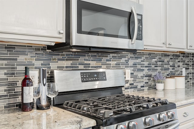 kitchen featuring white cabinetry, light stone counters, appliances with stainless steel finishes, and decorative backsplash