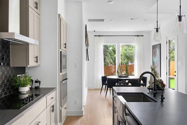 kitchen featuring light hardwood / wood-style floors, hanging light fixtures, wall chimney range hood, backsplash, and stainless steel appliances