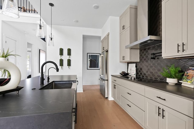 kitchen featuring high quality fridge, black electric stovetop, hanging light fixtures, sink, and wall chimney exhaust hood