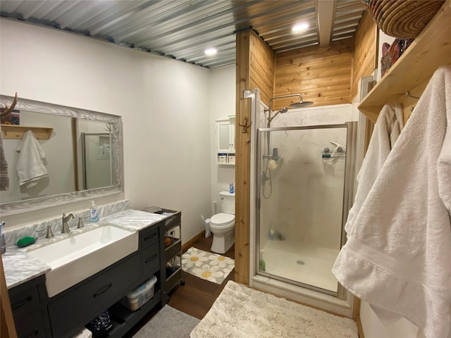 bathroom with toilet, a shower with door, wooden walls, and vanity