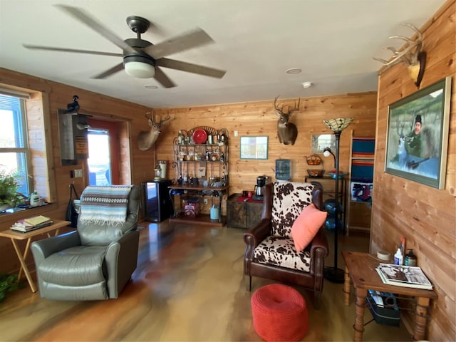 living area with ceiling fan and wooden walls