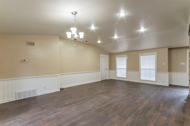 empty room with dark hardwood / wood-style floors, an inviting chandelier, and vaulted ceiling