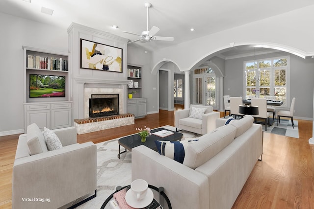 living room with ceiling fan, built in features, light wood-type flooring, a fireplace, and ornamental molding