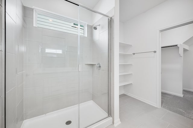 full bath with a spacious closet, tile patterned floors, a shower stall, and baseboards