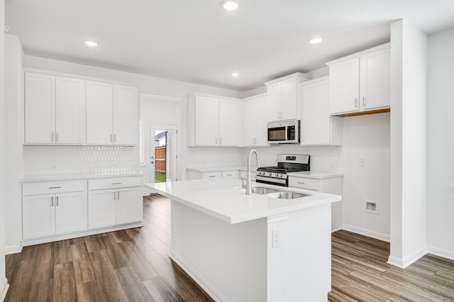 kitchen with wood finished floors, white cabinetry, light countertops, appliances with stainless steel finishes, and a center island with sink