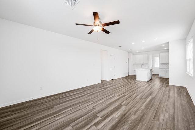 unfurnished living room featuring visible vents, ceiling fan, a sink, wood finished floors, and baseboards