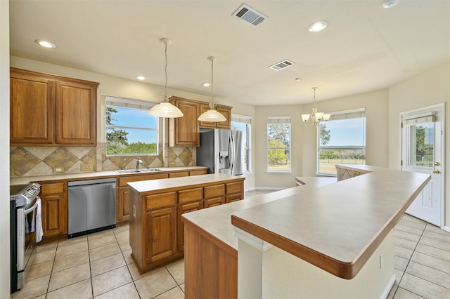 kitchen with light tile patterned flooring, appliances with stainless steel finishes, backsplash, hanging light fixtures, and a center island